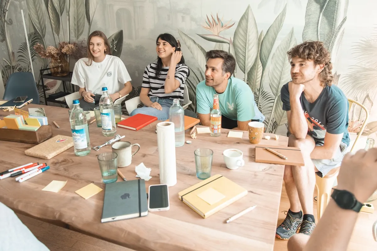 The Lively Apps team gathered in their office conference room, sitting around a wooden table during a casual team meeting with notebooks, drinks, and brainstorming materials.